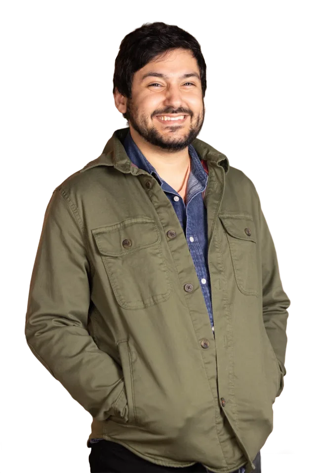 Daniel smiling in an olive jacket and denim shirt, hands in his pockets